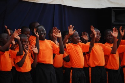 Children's choir singing, smiling and with arms raised